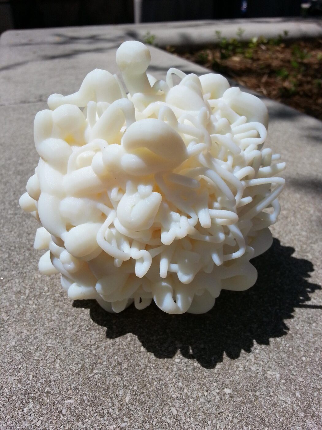 A white 3D-printed Protobyte rootball, a tangle of tubular forms, photographed on concrete in sunlight